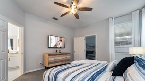 Un dormitorio con cama, ventilador de techo, televisor, cómoda y armario.