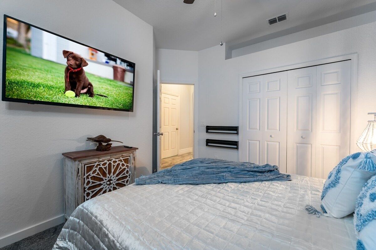 Ein Schlafzimmer mit einem Bett, einem an der Wand befestigten Fernseher, einer Tür und einem Schrank.