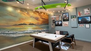 Una habitación con un mural de playa, una mesa de fútbol y tablas de surf colgadas del techo.