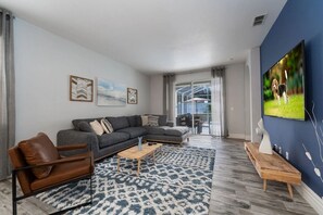 Ein modernes Wohnzimmer mit einer Eckcouch, einem braunen Ledersessel, einem Couchtisch und einem an einer blauen Wand montierten Fernseher.