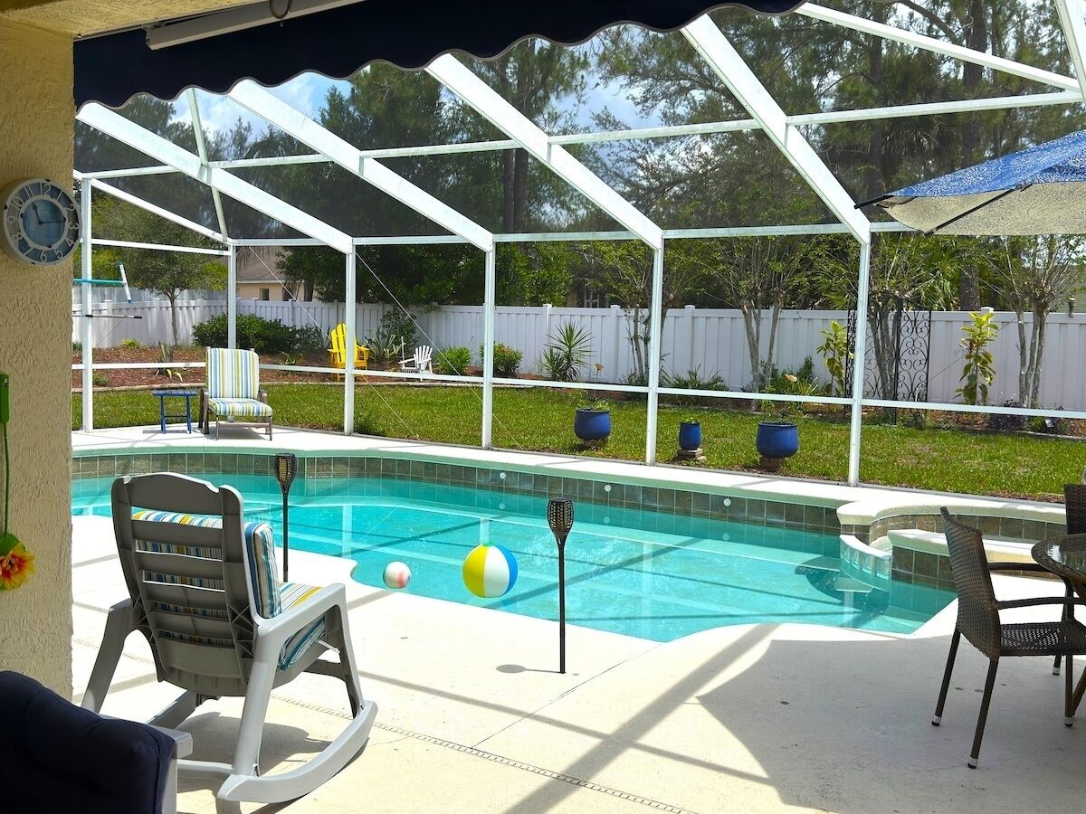 A covered outdoor swimming pool area with lounge chairs and a table.