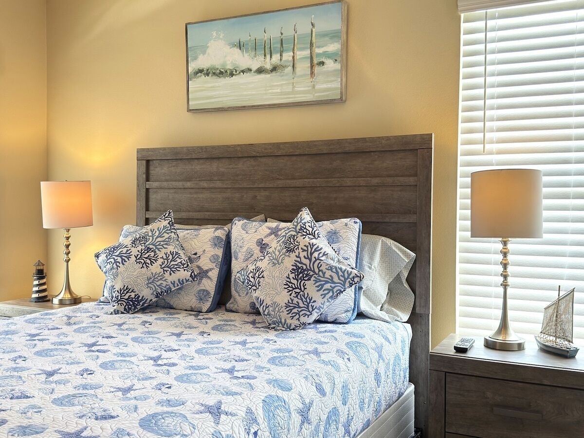 A bedroom with a bed, two lamps, a nightstand, and a painting on the wall.