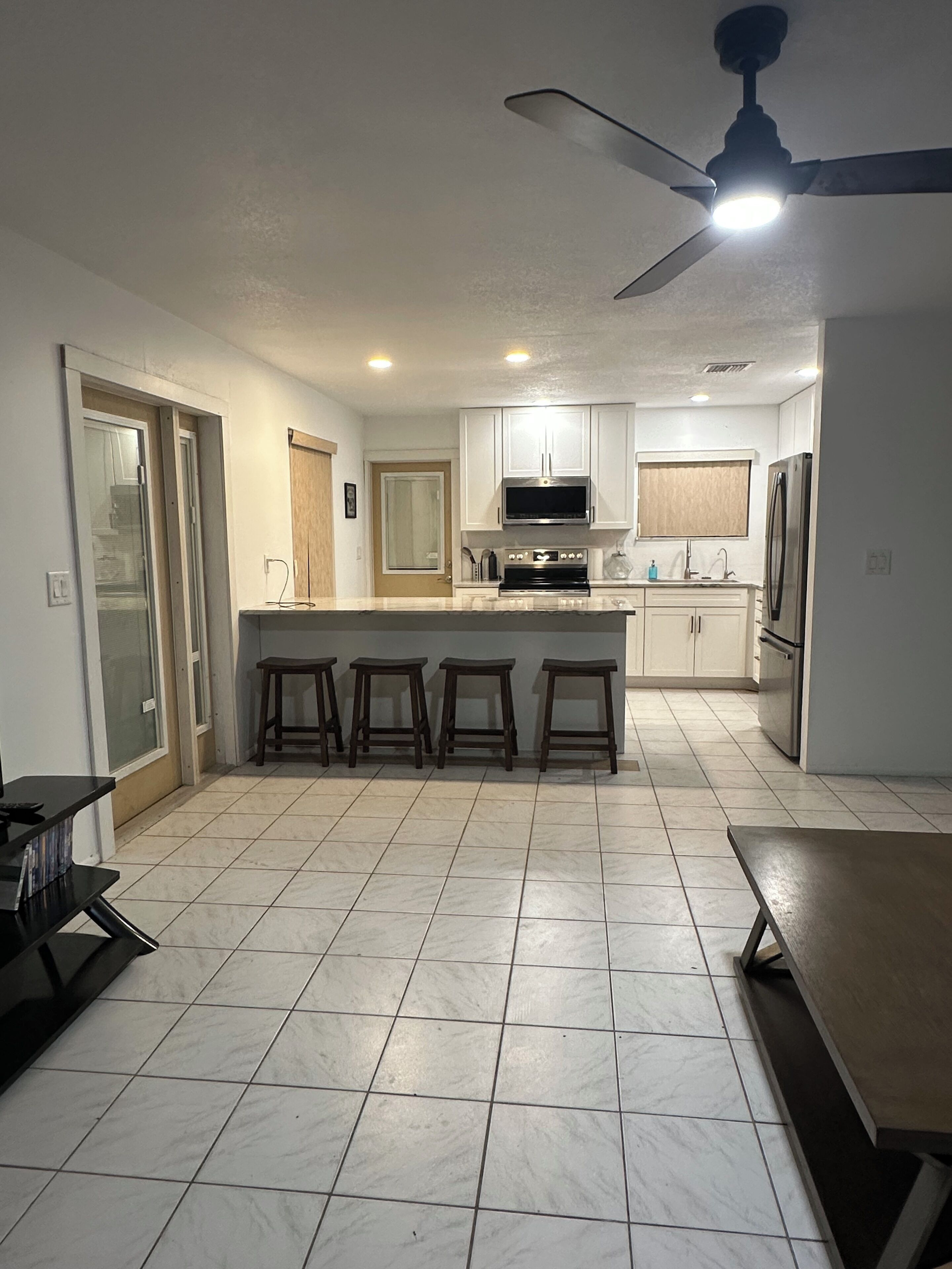 A modern kitchen with a central island, bar stools, and a ceiling fan.