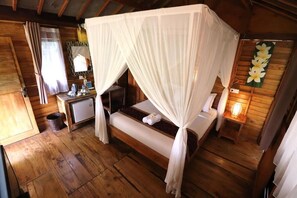 A wooden room with a bed under a canopy, a desk with a chair, a small table with a lamp, and a wall-mounted mirror. - Hidden gem Superior Bungalow at Ubud (Ubud)