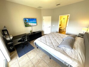 Ein Schlafzimmer mit einem Bett, einem Schreibtisch, einem Sessel, einem Fernseher und einer Tür zu einem Badezimmer.