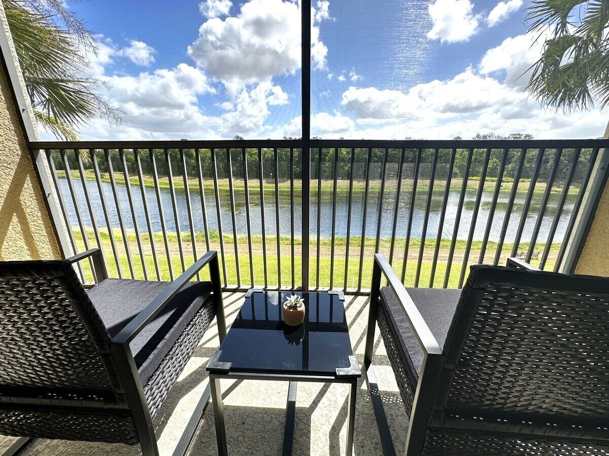 A balcony with a view of a lake, two chairs, and a small table with a plant.