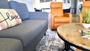 A modern living room with a grey sofa, an orange armchair, a round wooden coffee table, and a world map on the wall.