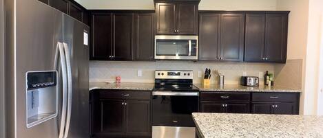 A modern kitchen with dark cabinets, stainless steel appliances, and granite countertops.