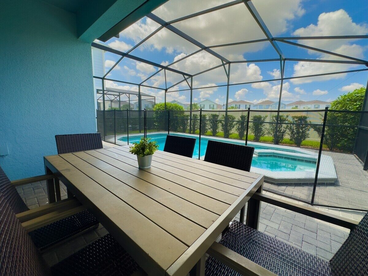 Un espace extérieur aménagé avec des sièges, protégé du soleil, et une piscine en arrière-plan.