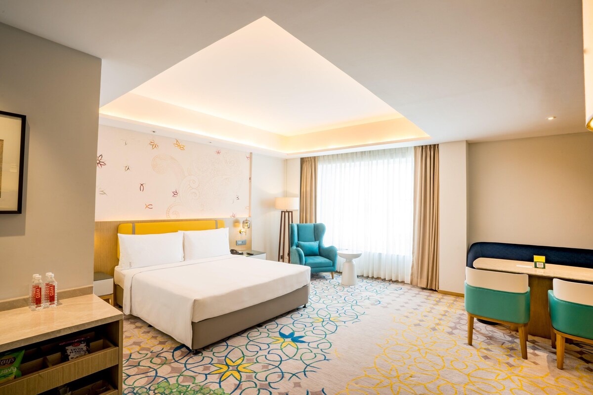 A hotel room with a bed, a desk, a chair, a small table, and a patterned carpet.