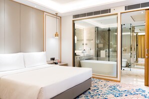 Una habitación de hotel moderna con una cama grande, ducha con cerramiento de vidrio y baño independiente.