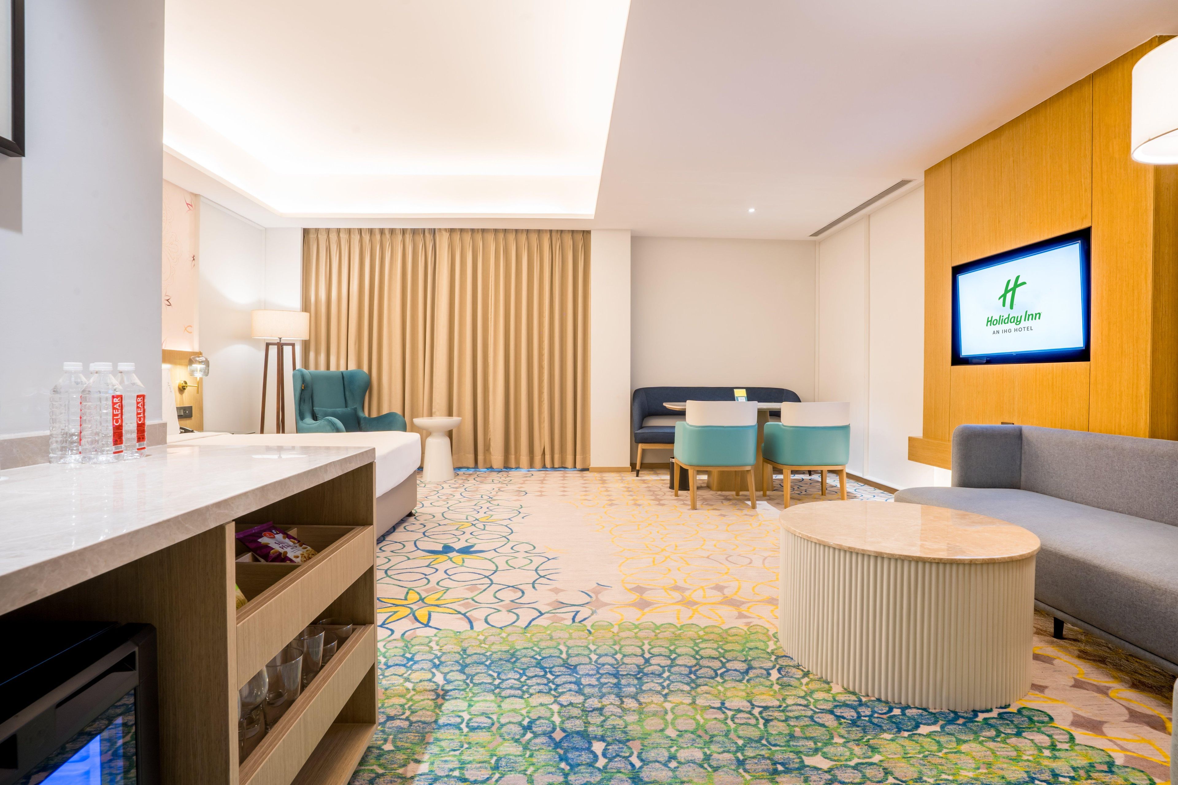 A hotel room with a bed, a desk, a TV, a sofa, and a patterned carpet.