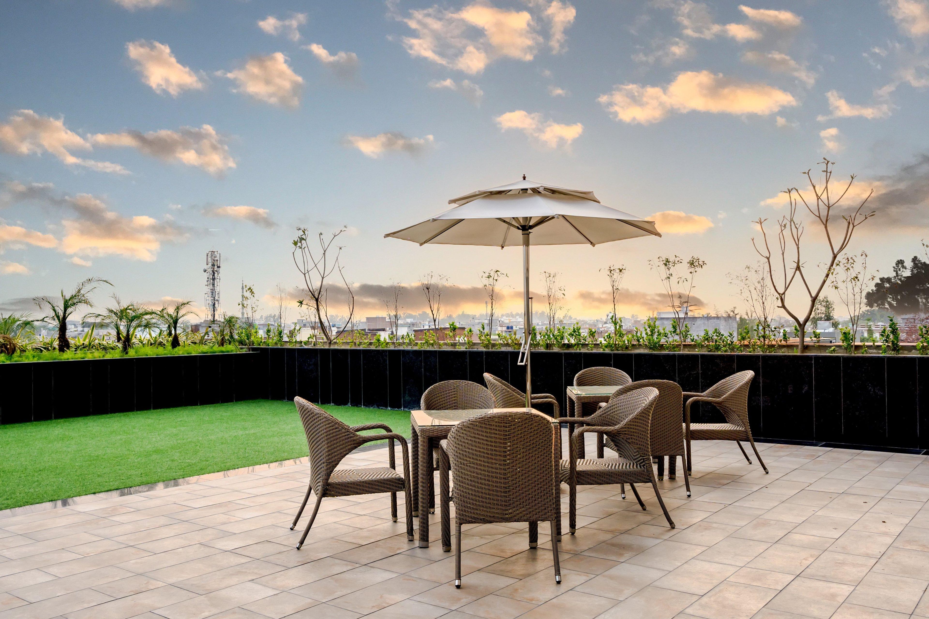 An outdoor patio with wicker furniture and a table, a large umbrella, and a view of the city skyline.