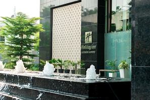 A modern building with a waterfall feature, Holiday Inn signage, and potted plants.