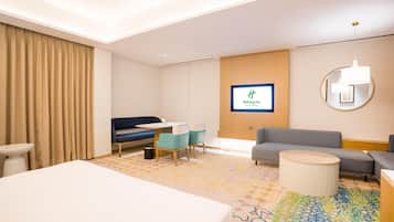 Ett hotellrum med en säng, ett skrivbord med en stol, en soffa, ett runt soffbord, en tv och en mönstrad matta.