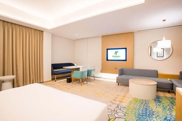 Une chambre d’hôtel comprenant un lit, un bureau avec une chaise, un canapé, une table basse ronde, un téléviseur et une moquette à motifs.