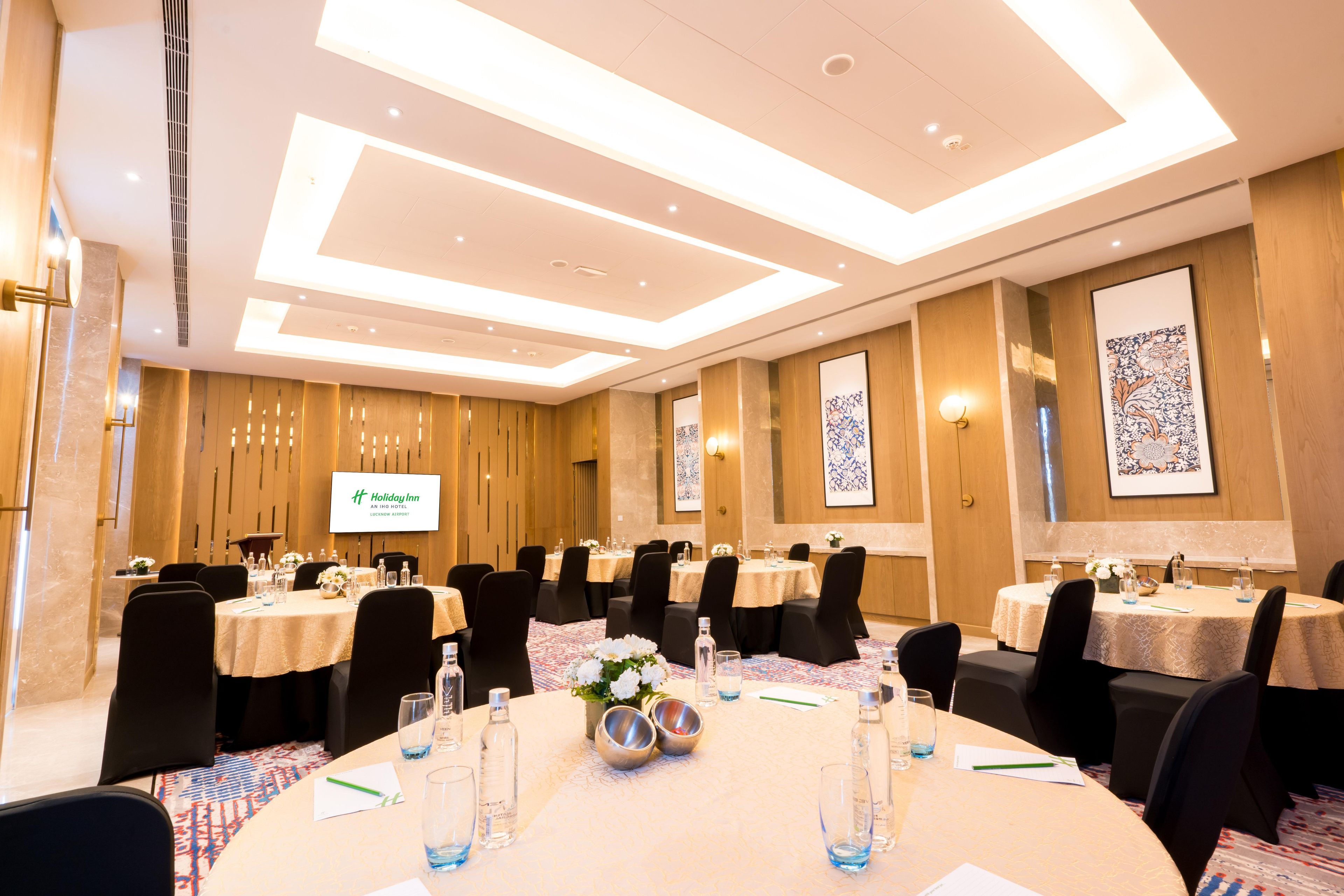 A conference room with multiple tables, chairs, and a presentation screen.