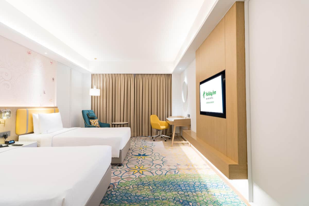 Ein Hotelzimmer mit zwei Betten, einem Schreibtisch, einem Stuhl, einem Fernseher und einem gemusterten Teppich.