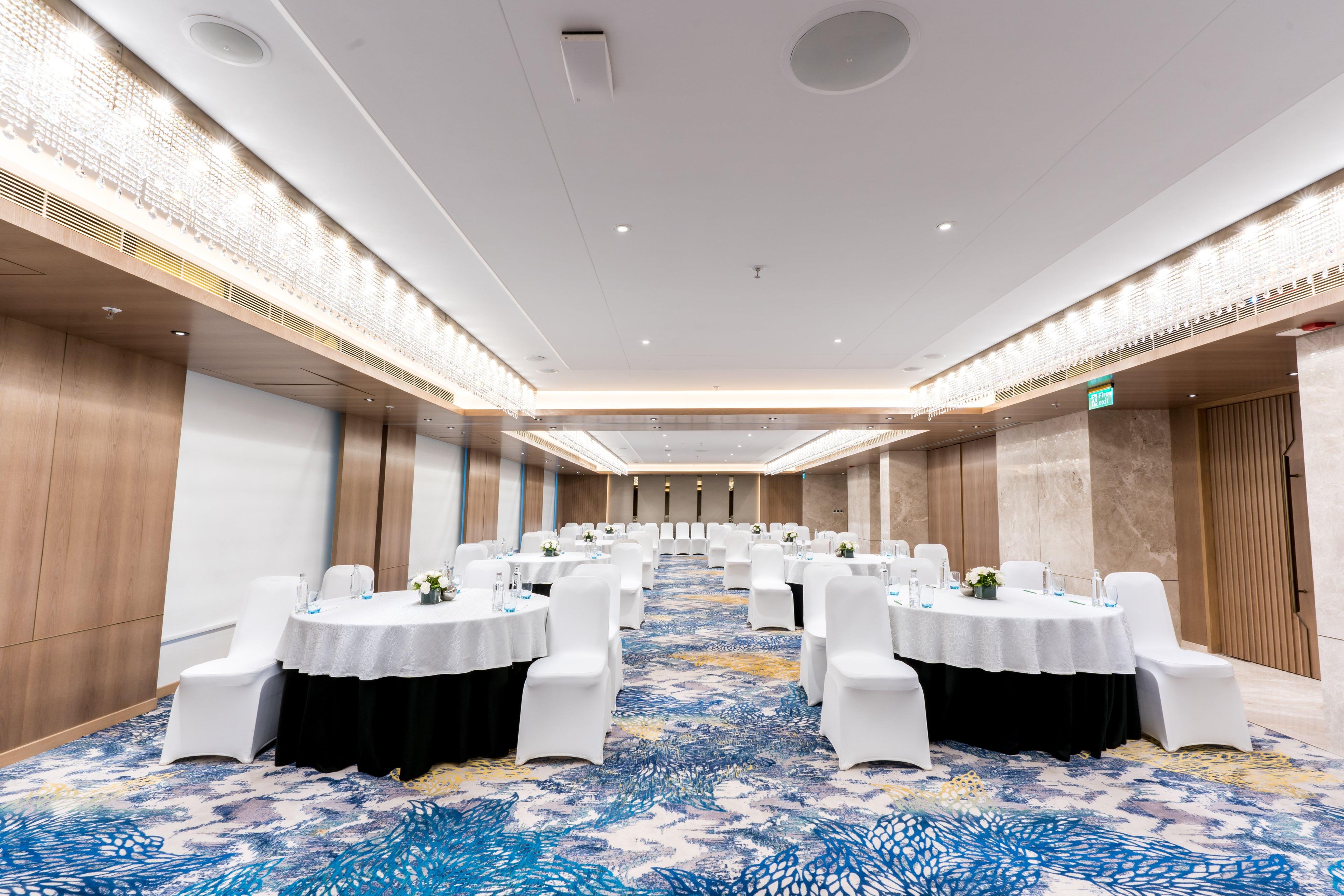 A conference room with round tables, white chairs, and a patterned carpet.