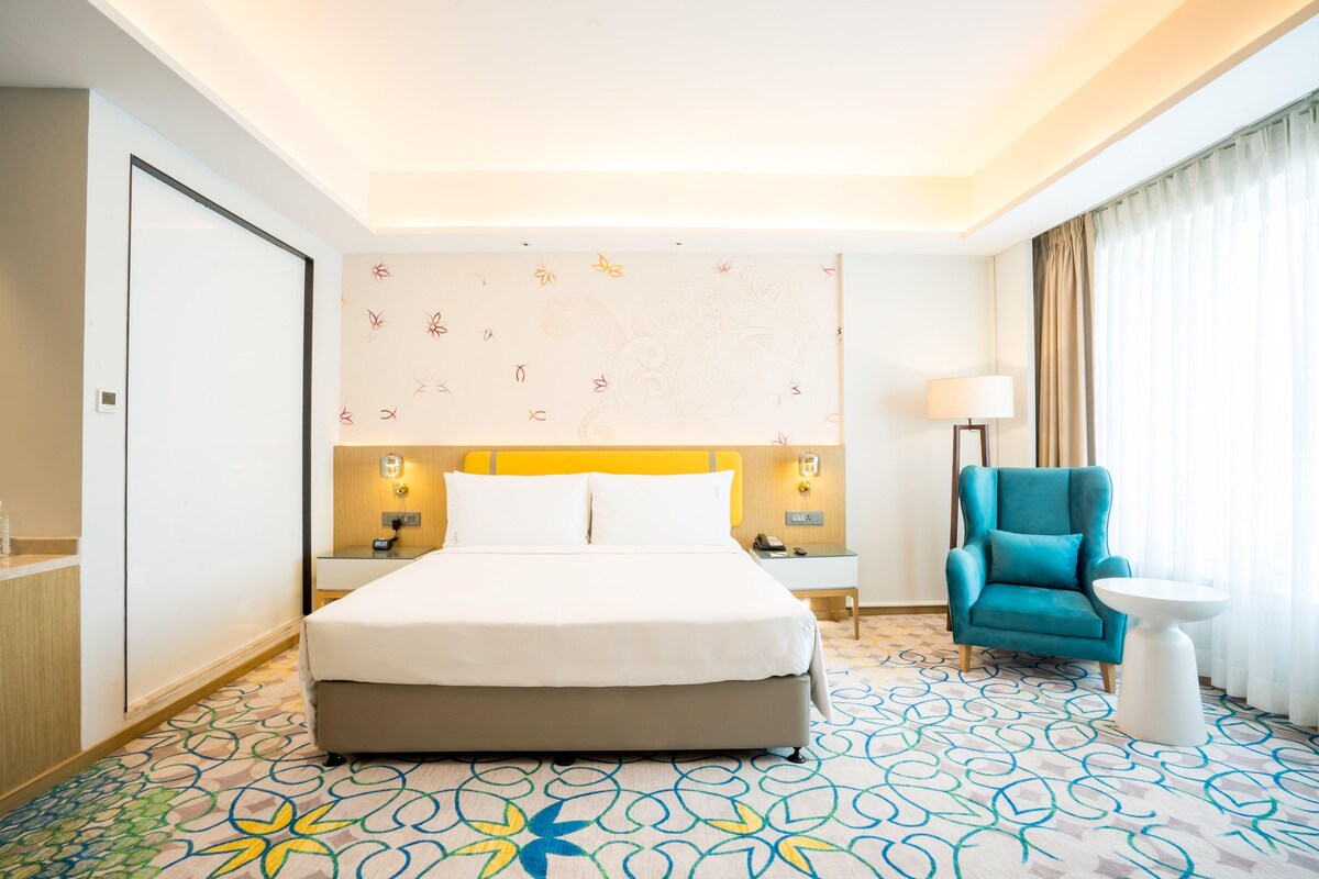 Ein Hotelzimmer mit Bett, Nachttisch, Lampe, Stuhl und kleinem Tisch.