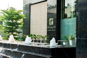 A modern building with a waterfall feature, Holiday Inn signage, and potted plants. - Holiday Inn Lucknow Airport (Lucknow)