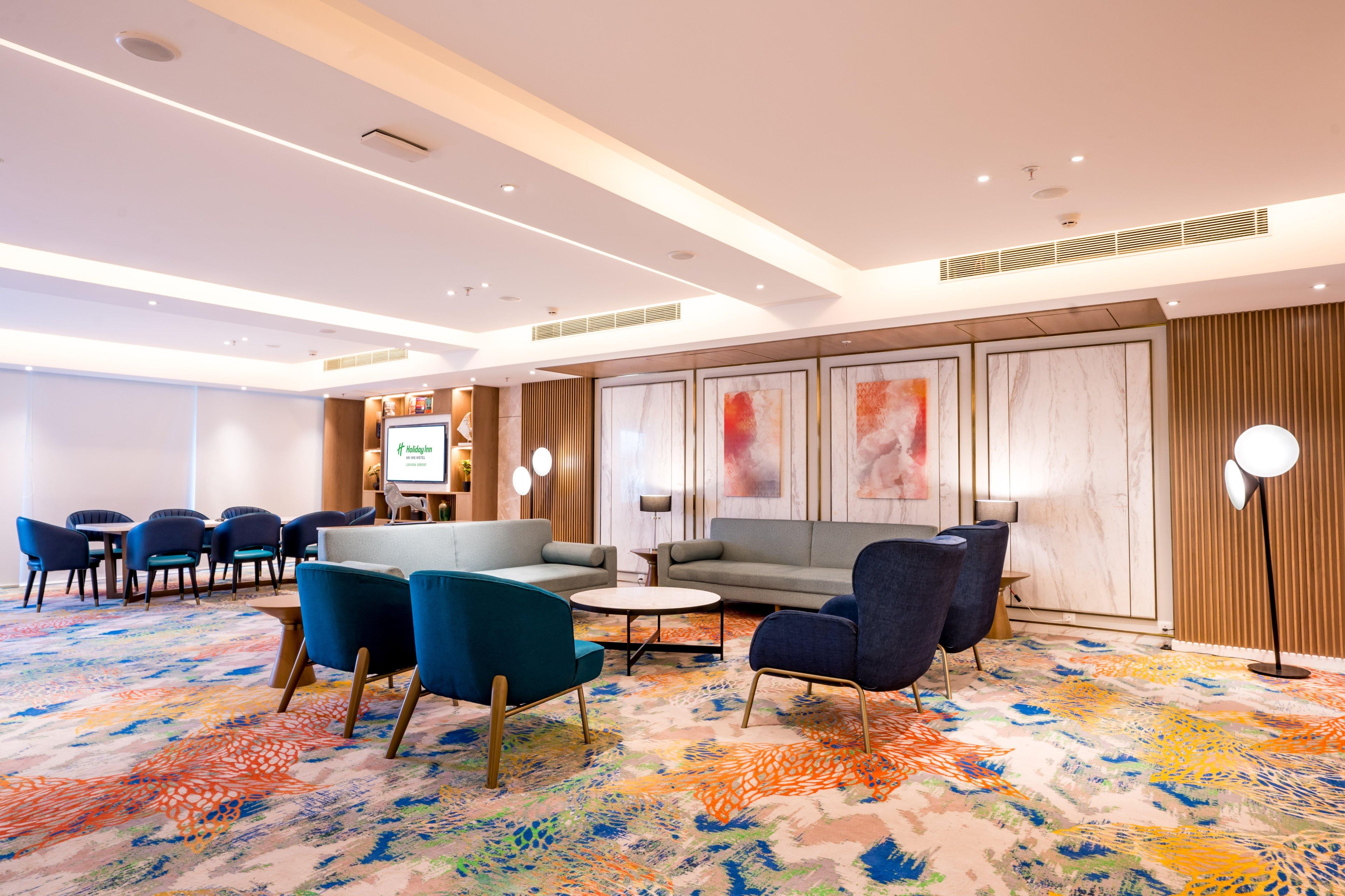 A hotel lobby with a seating area, a TV screen, and a patterned carpet.