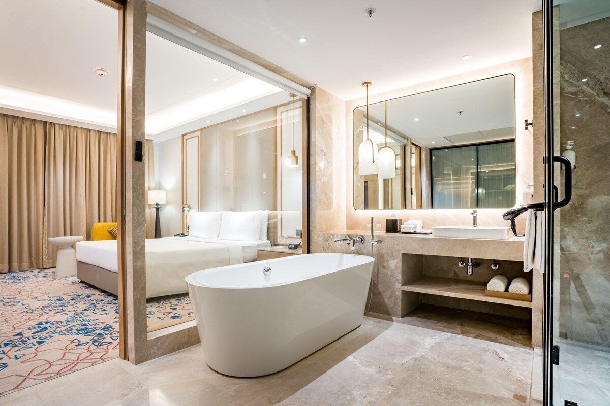 A modern hotel bathroom with a freestanding bathtub, a large mirror, and a separate shower area.