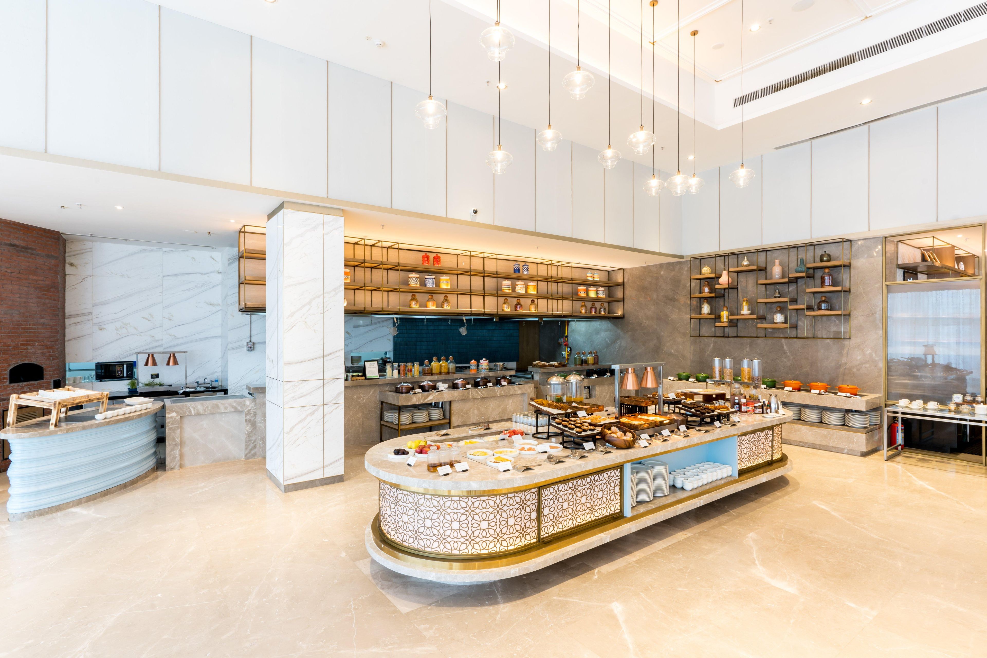 A modern kitchen with marble countertops, a central island with food items, and built-in shelves with kitchenware.