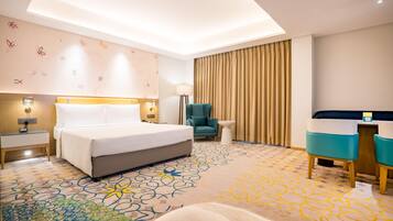 A hotel room with a bed, a desk, a chair, a lamp, and a patterned carpet.