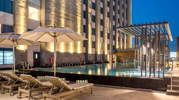 A pool area with lounge chairs and umbrellas, a lifebuoy, and a building with a modern design.
