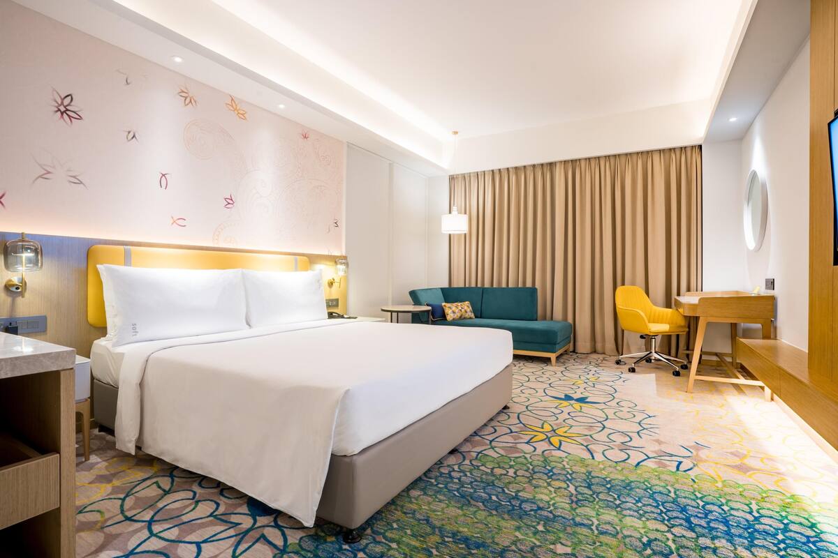 A hotel room with a bed, a desk, a chair, a sofa, and a patterned carpet.
