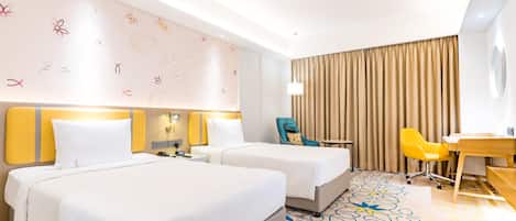 A hotel room with two beds, a desk, a chair, and a patterned carpet.