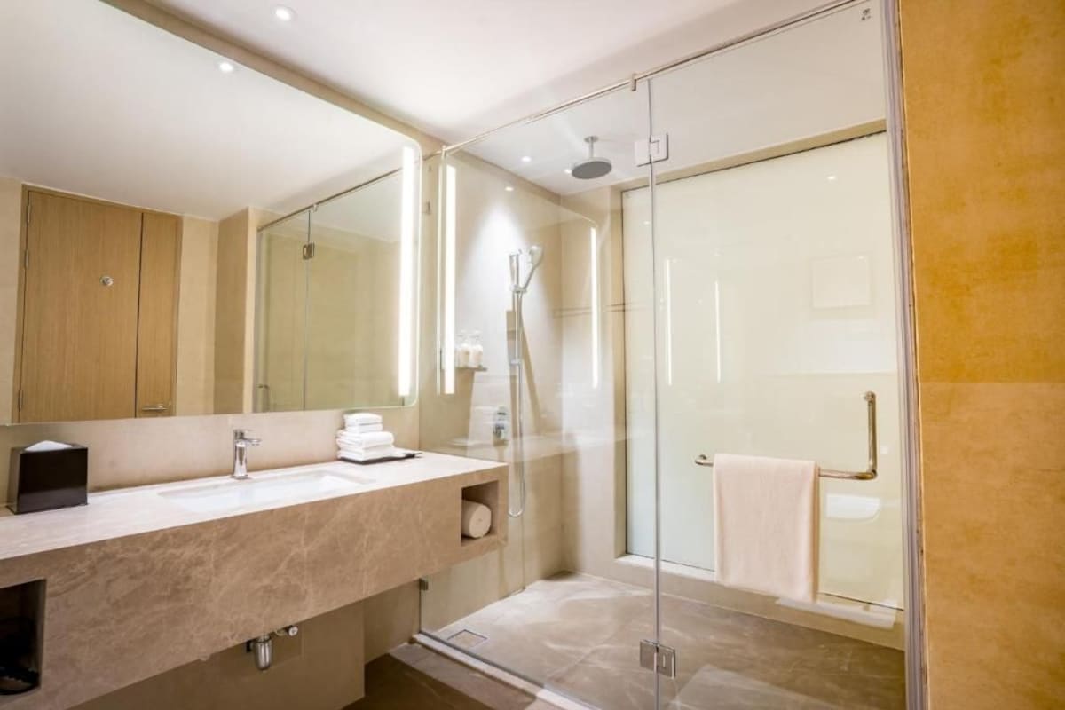 A modern bathroom with a glass-enclosed shower, a large mirror, and a marble countertop.