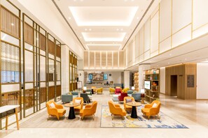 A spacious lobby with multiple seating areas, a reception desk, and a television screen. - Holiday Inn Lucknow Airport (Lucknow)