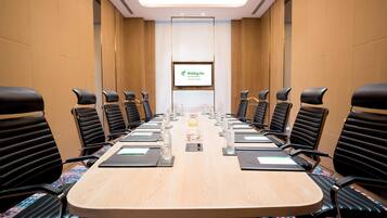 Een vergaderzaal met een lange tafel, zwarte stoelen en een scherm waarop het Holiday Inn logo staat.