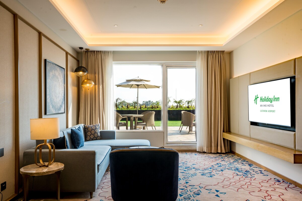 Een hotelkamer met een bank, een ronde tafel, een televisie en uitzicht op het buiten.