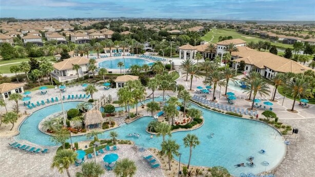 A large, winding pool surrounded by palm trees and lounge chairs, with a golf course in the background. - 6 Bd Luxury Villa In Championsgate With Private Pool 6 Bedroom Home (Davenport)