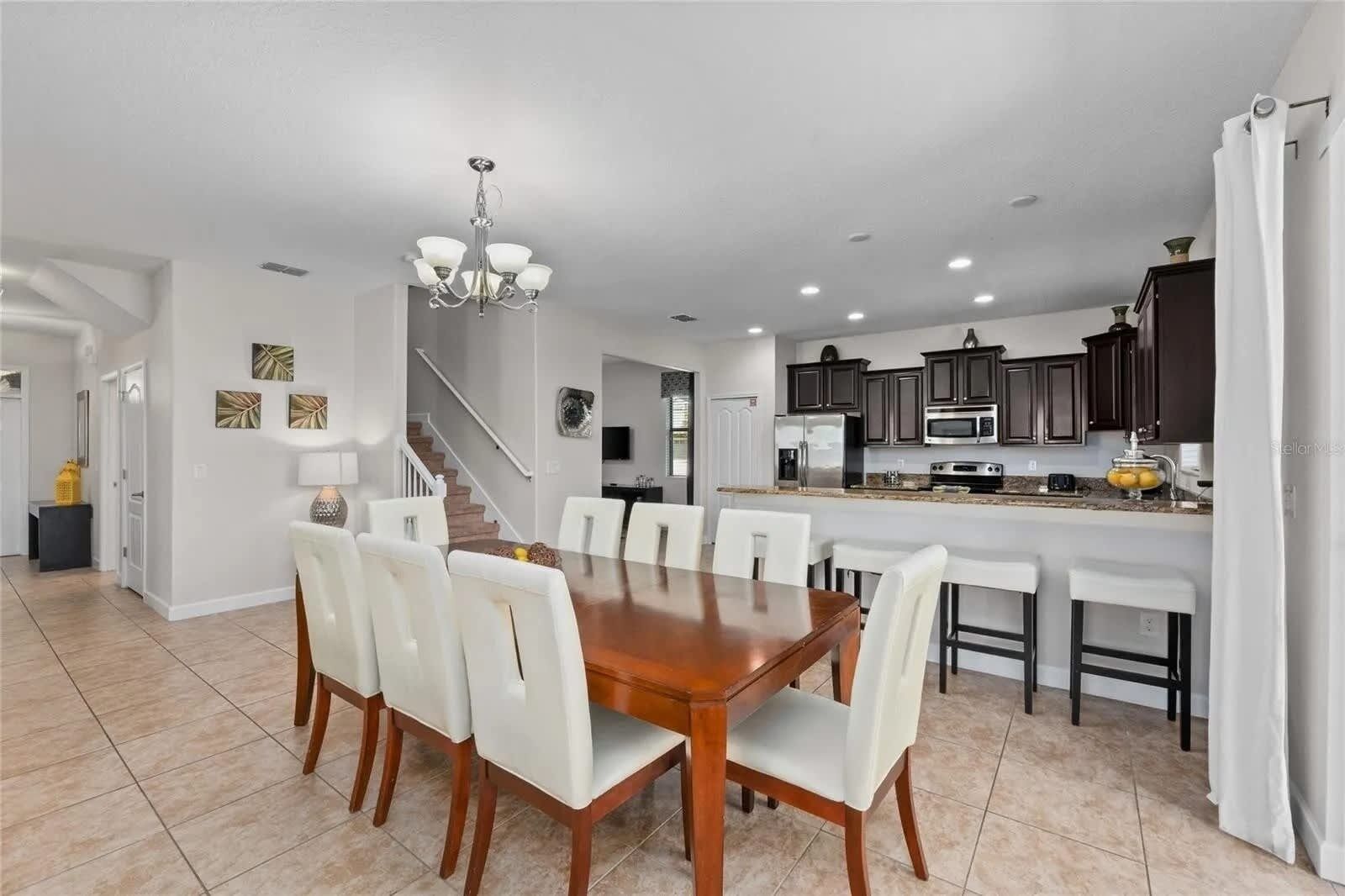 A spacious kitchen with dark cabinets, a central island, and a dining area with a wooden table and white chairs.