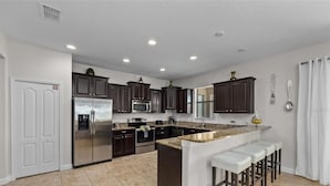 A modern kitchen with dark cabinets, stainless steel appliances, and a granite countertop. - 6 Bd Luxury Villa In Championsgate With Private Pool 6 Bedroom Home (Davenport)