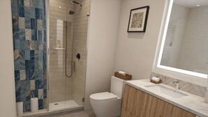 A modern bathroom with a glass-enclosed shower, a toilet, and a vanity with a large mirror.