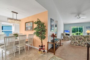 A living room with a dining area, a ceiling fan, a large plant, and a television. - Minutes From Disney Themed 2 Bd Villa With Private Pool 2 Bedroom Home (Kissimmee)