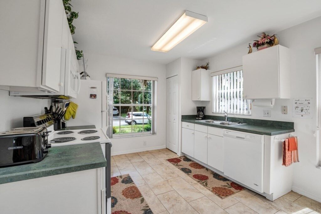 A kitchen with white cabinets, a stove, a sink, and a window with a view of the outside.