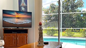 Sala de estar com uma mesa de madeira, televisão e vista para uma piscina.