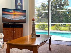 A living room with a wooden table, a television, and a view of a swimming pool. - Minutes From Disney Themed 2 Bd Villa With Private Pool 2 Bedroom Home (Kissimmee)