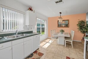 A kitchen with white cabinets, a double sink, and a dining area with a table and chairs. - Minutes From Disney Themed 2 Bd Villa With Private Pool 2 Bedroom Home (Kissimmee)