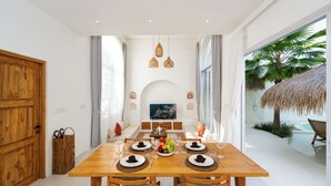 Zona pranzo con tavolo in legno apparecchiato per quattro persone, televisione sullo sfondo e vista sulla piscina.