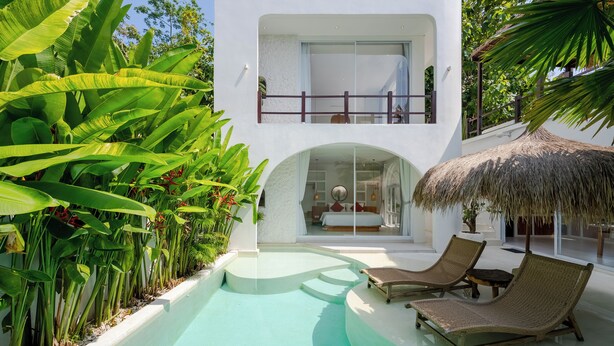 Una villa moderna con piscina, lettini e rigogliosa vegetazione tropicale.
