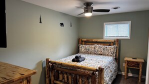 Quarto com cama de madeira, ventilador de teto, janela com persianas e mesinhas de cabeceira de madeira.