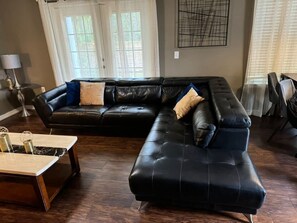 Ein Wohnzimmer mit einer schwarzen Ledersofa, einem Holztisch und einer Stehlampe.