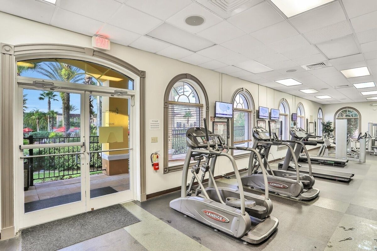 A fitness center with treadmills, a fire extinguisher, and a view of palm trees outside.